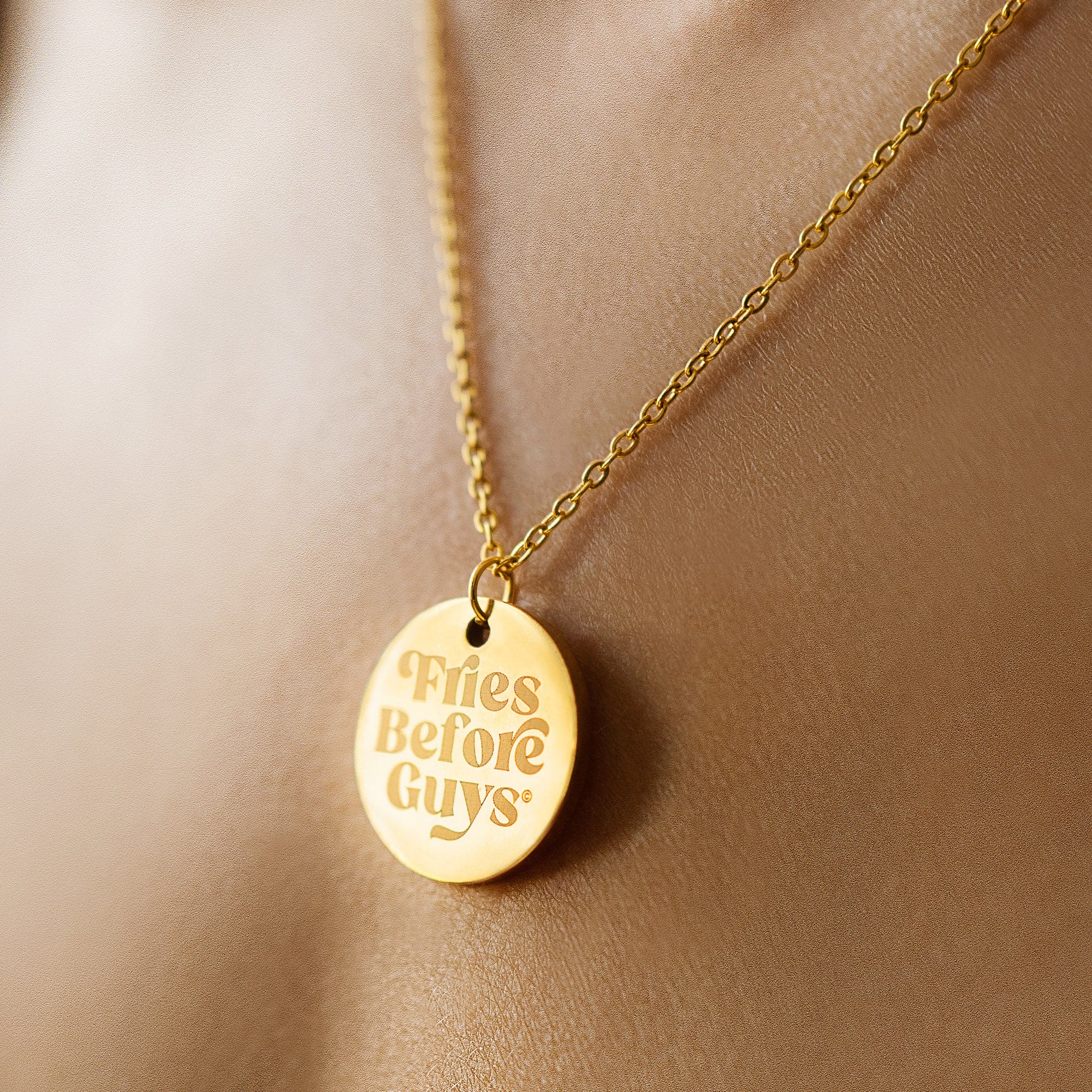 Nahaufnahme von goldenee Kette mit rundem "Fries Before Guys"-Anhänger