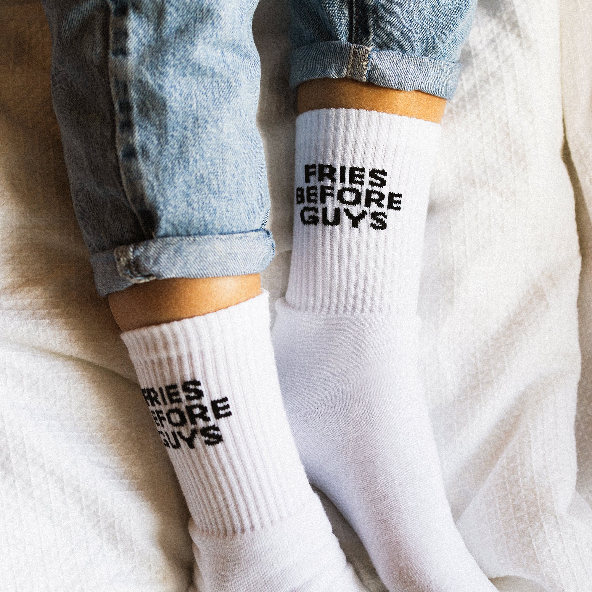 Weiße Sportsocken mit schwarzem "Fries Before Guys" Stick auf einer weißen Decke