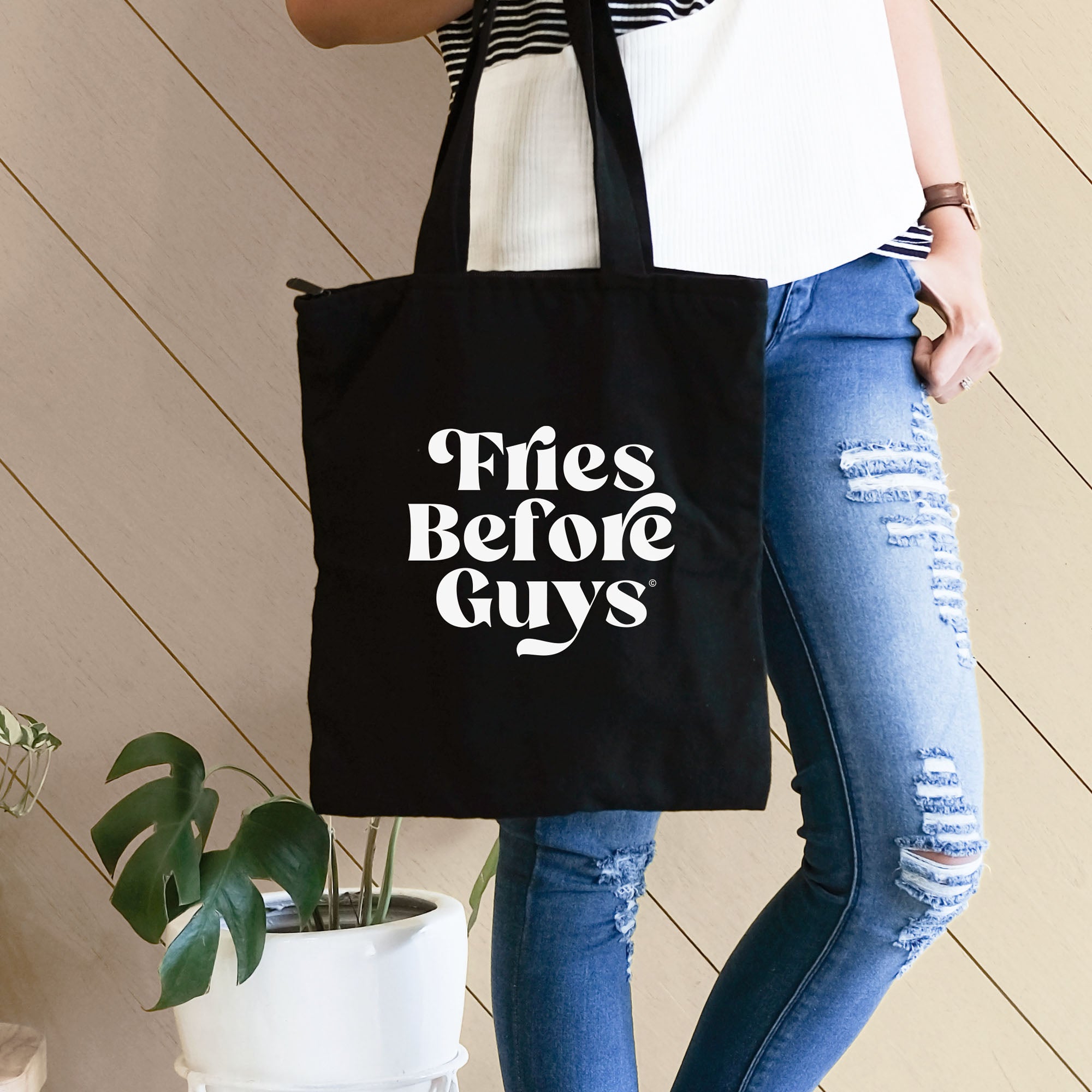 Frau trägt schwarze Tragetasche mit weißem "Fries Before Guys"-Druck zu einem lockeren Outfit.