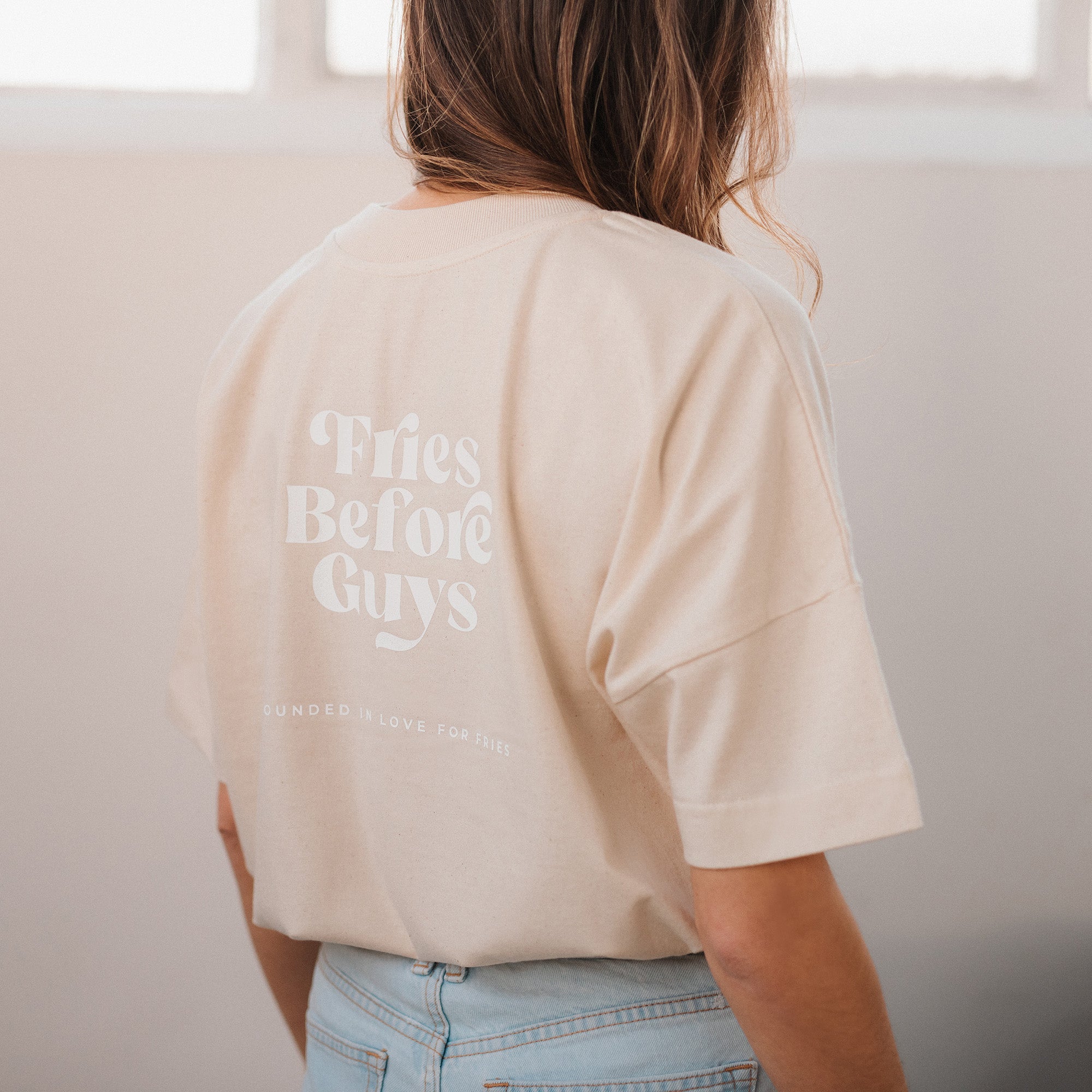 Frau trägt vanillafarbenes T-Shirt mit großem "Fries Before Guys"-Rückenprint.