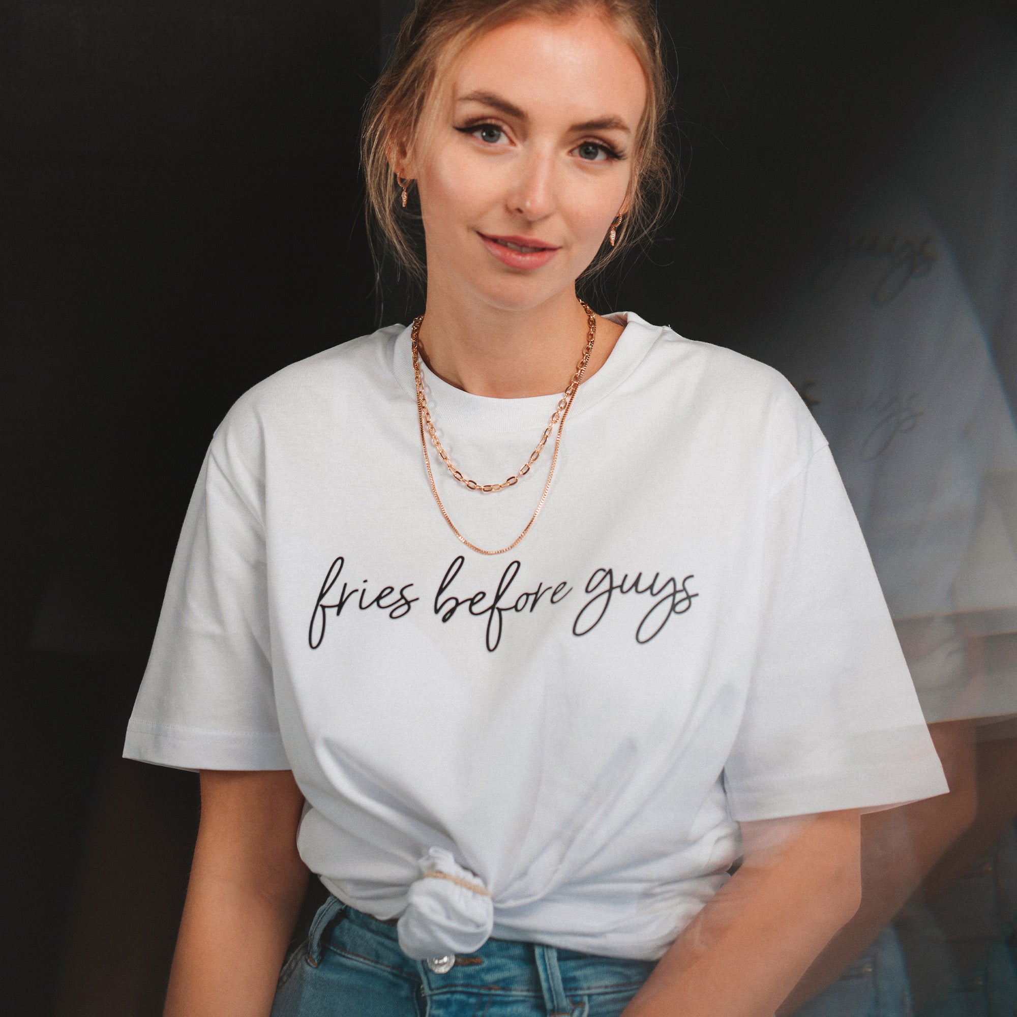 Frau trägt weißes T-Shirt mit schwarzem "Fries Before Guys"-Druck, das vorne zusammengeknotet wurde