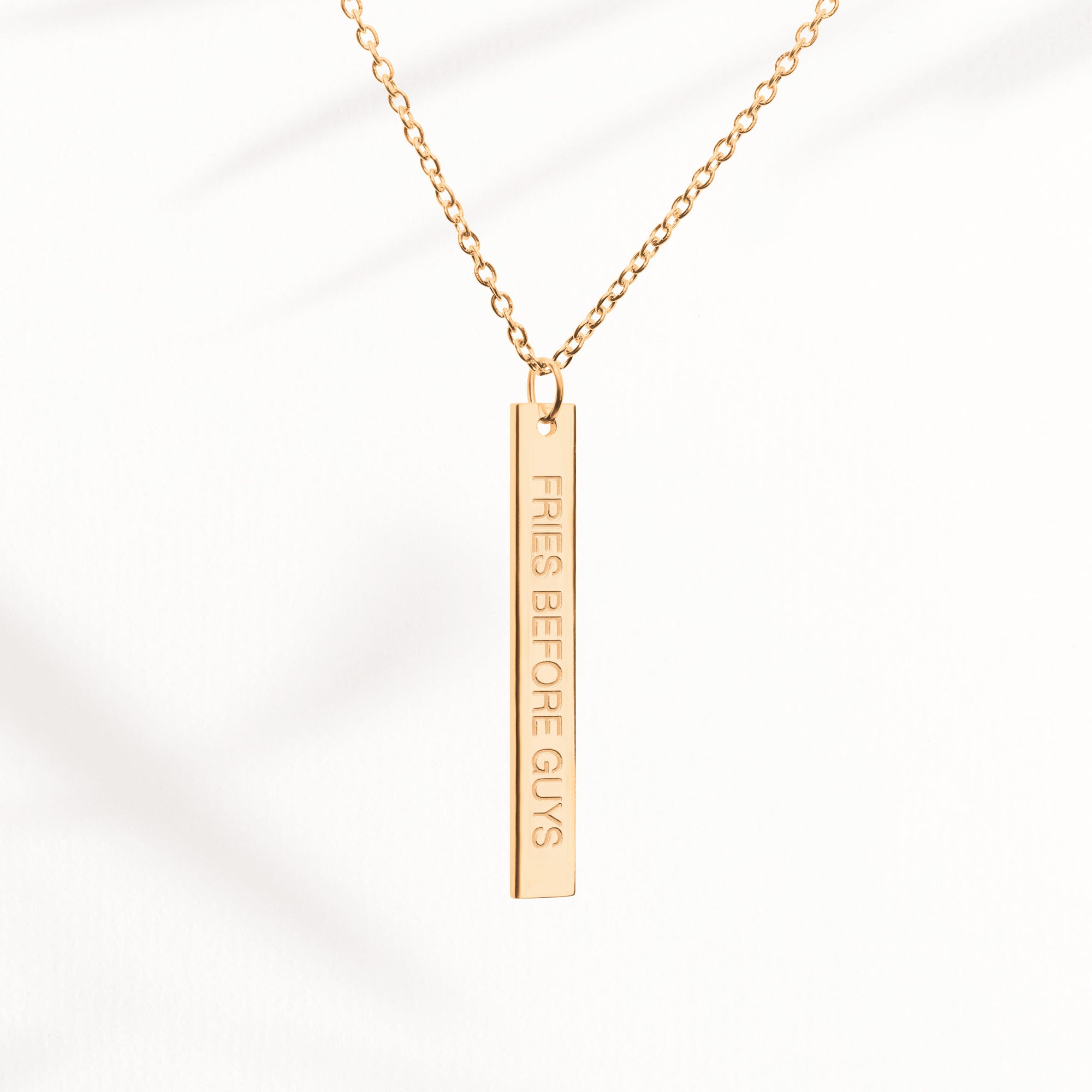 Goldene Kette mit länglichem Anhänger und "Fries Before Guys"-Gravur auf der Vorderseite.