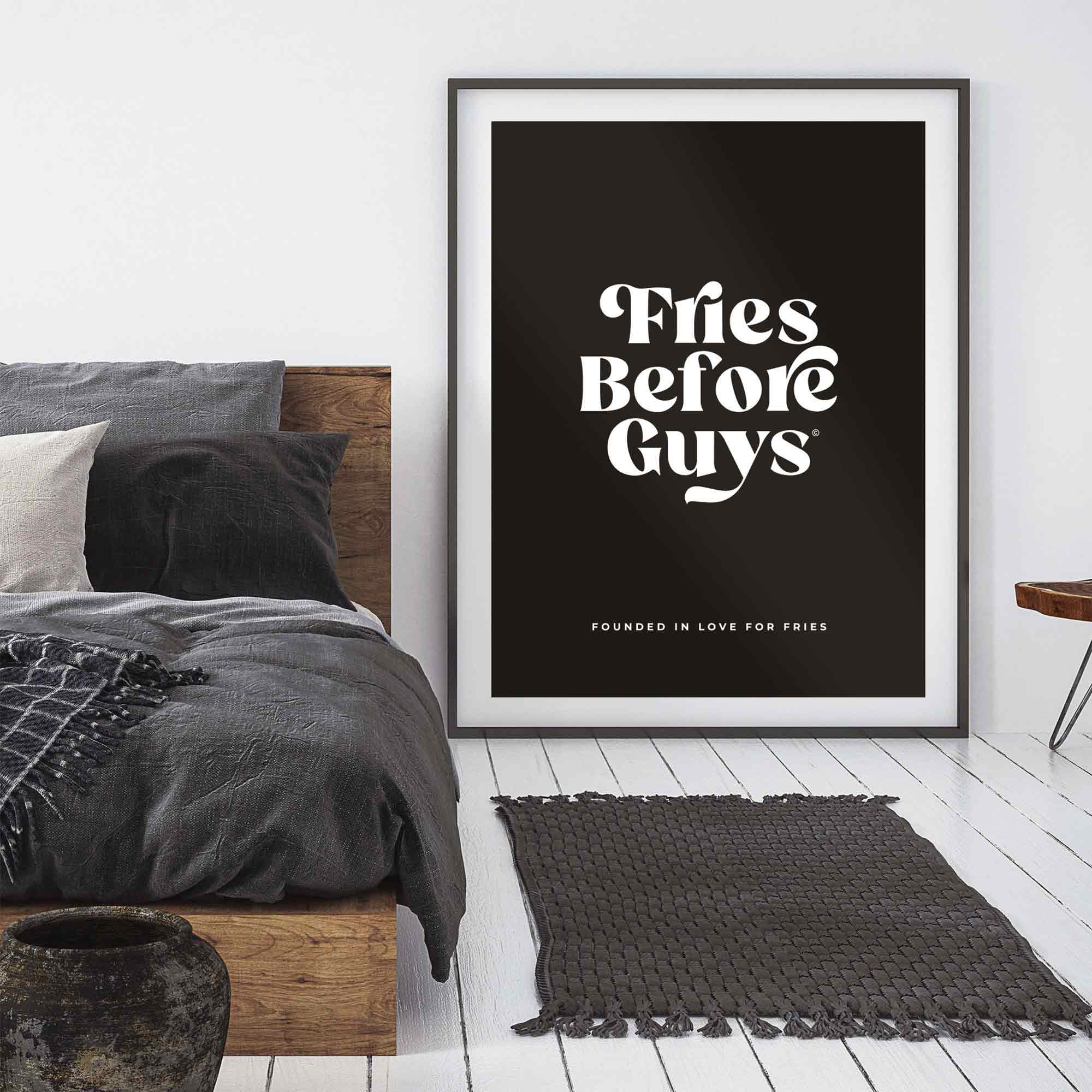 Schwarzes Poster mit weißem "Fries Before Guys"-Spruch in schwarzem Rahmen neben Schlafzimmermöbeln