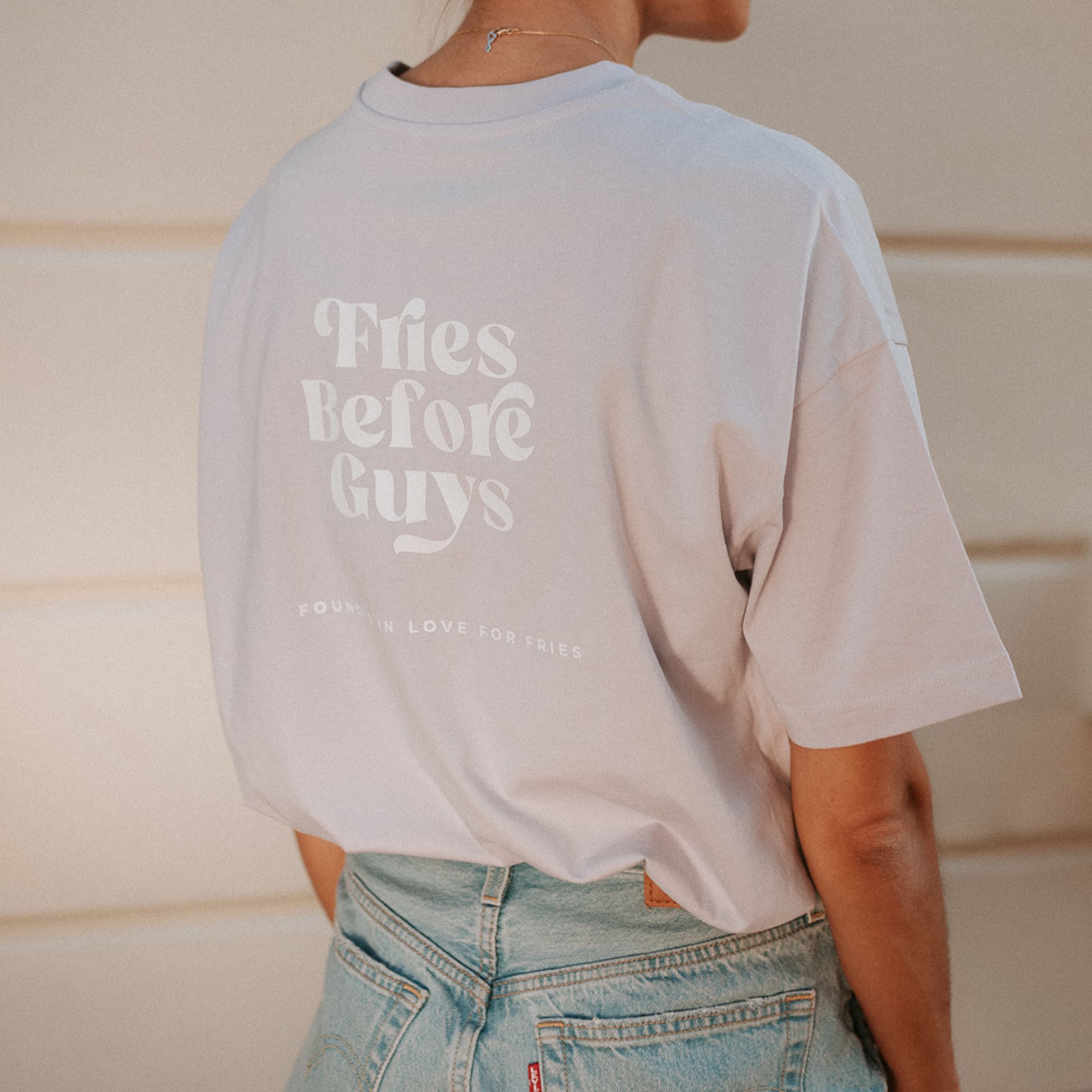 Rückenansicht von lilanem T-Shirt mit großem weißen "Fries Before Guys"-Print
