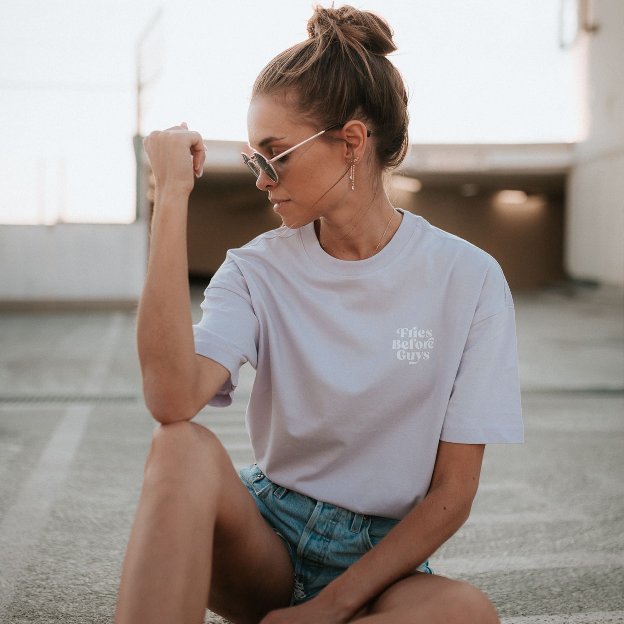 Frau sitzt in lilanem T-Shirt mit kleinem weißen "Fries Before Guys Druck" auf dem Boden