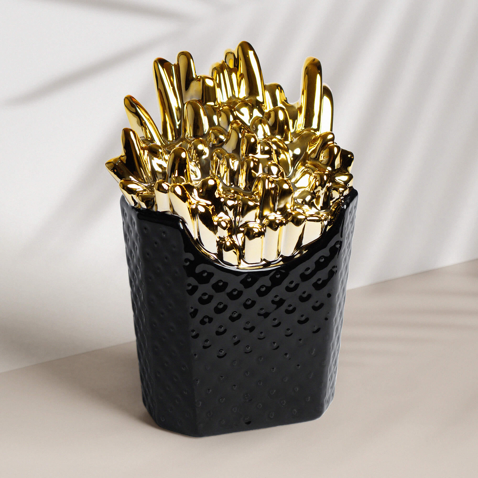 Spardose aus Keramik in Form einer schwarzen Pommestüte mit goldenen Pommes.