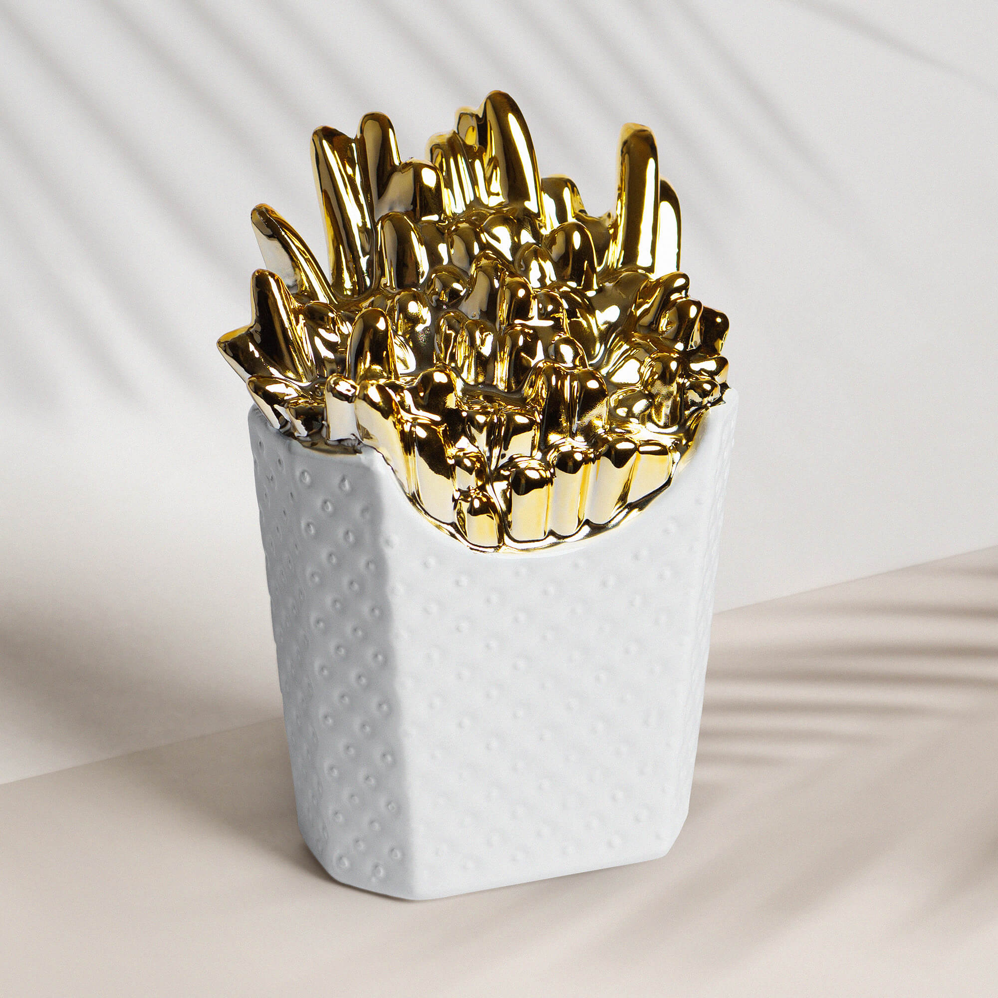 Spardose aus Keramik in Form einer weißen Pommestüte mit goldenen Pommes.