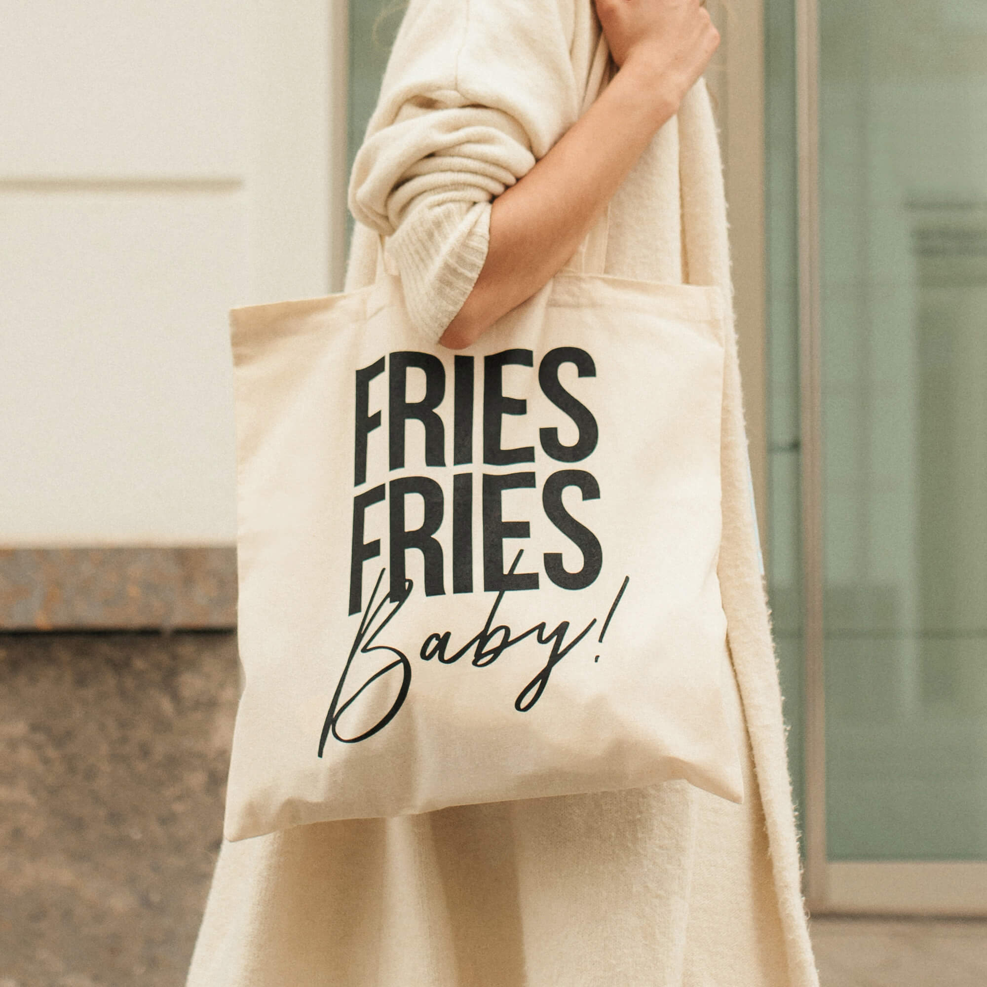 Frau in beigem Outfit trägt Tragetasche mit schwarzem "Fries Fries Baby"-Druck.